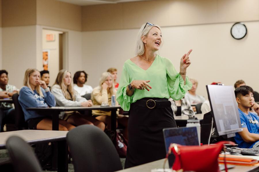 Doane teacher smiling and pointing off-screen in a class of students.